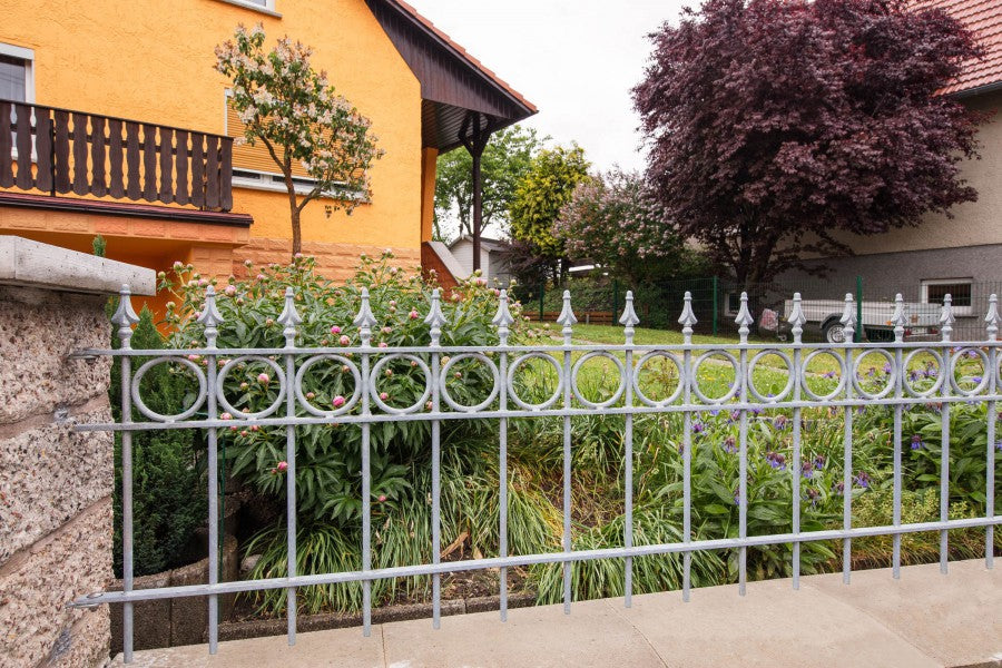 Zaun Belluno vor einem grünen Garten mit einem gelben Haus montiert | Feuerverzinkt